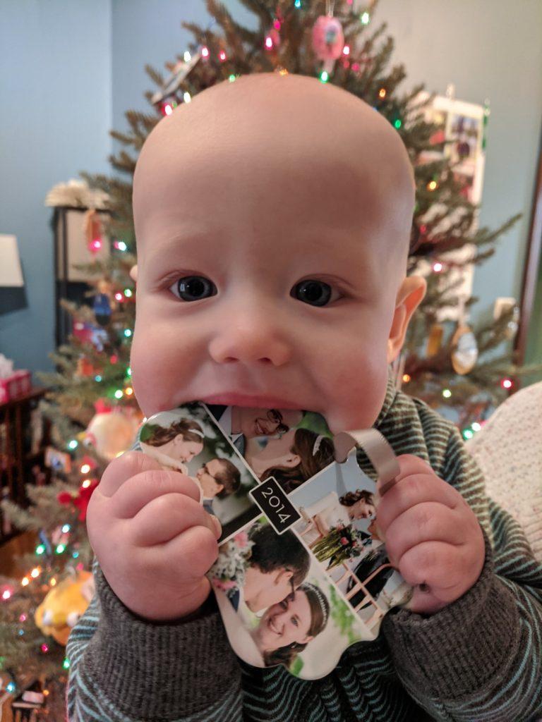 6-month-old boy with a Christmas ornament in his mouth that features wedding photos