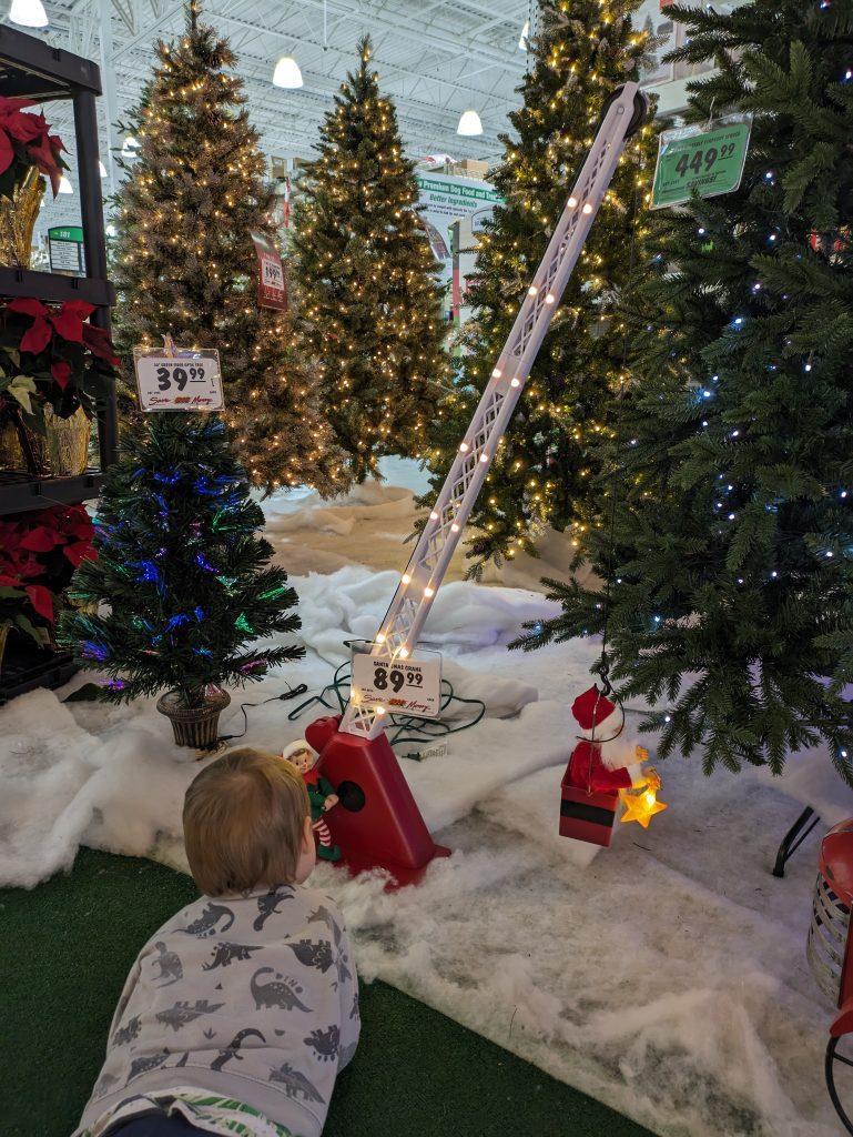 3-year-old boy laying on the floor of a store watching a Santa crane decoration go up and down