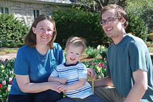 A mom, dad and toddler son sit in front of a blooming tulip garden