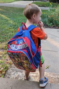 three-year-old boy wearing a Paw Patrol backpack standing on front porch looking out