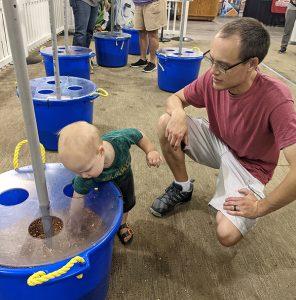 A man watches a baby play with corn kernels in a giant tub in the kid-friendly Agriland area