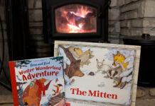 Two winter-themed books held up in front of a cheery fire in a wood-burning stove